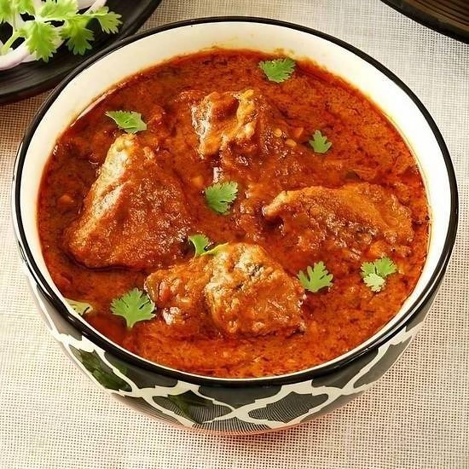 Bowl of chicken pieces in rich red curry sauce, garnished with fresh cilantro.