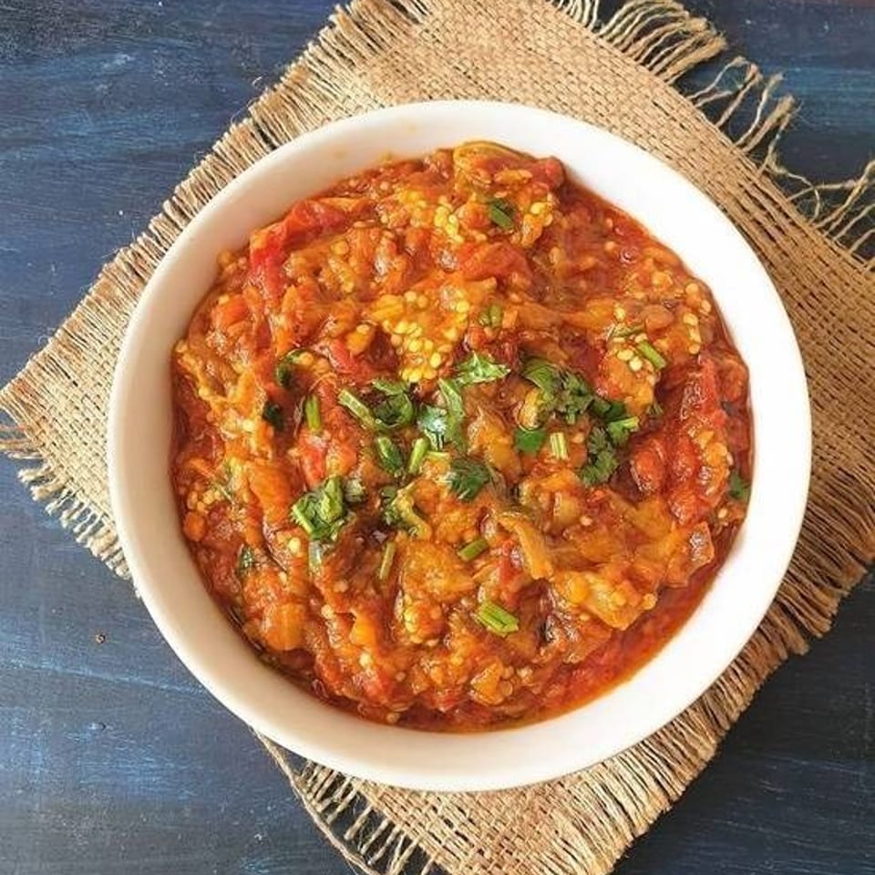 Bowl of chunky red tomato and pepper relish garnished with fresh herbs on a woven placemat.